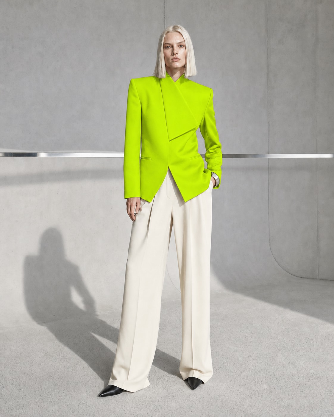 Fictional blonde fashion model in sculptural tailoring inside a concrete studio