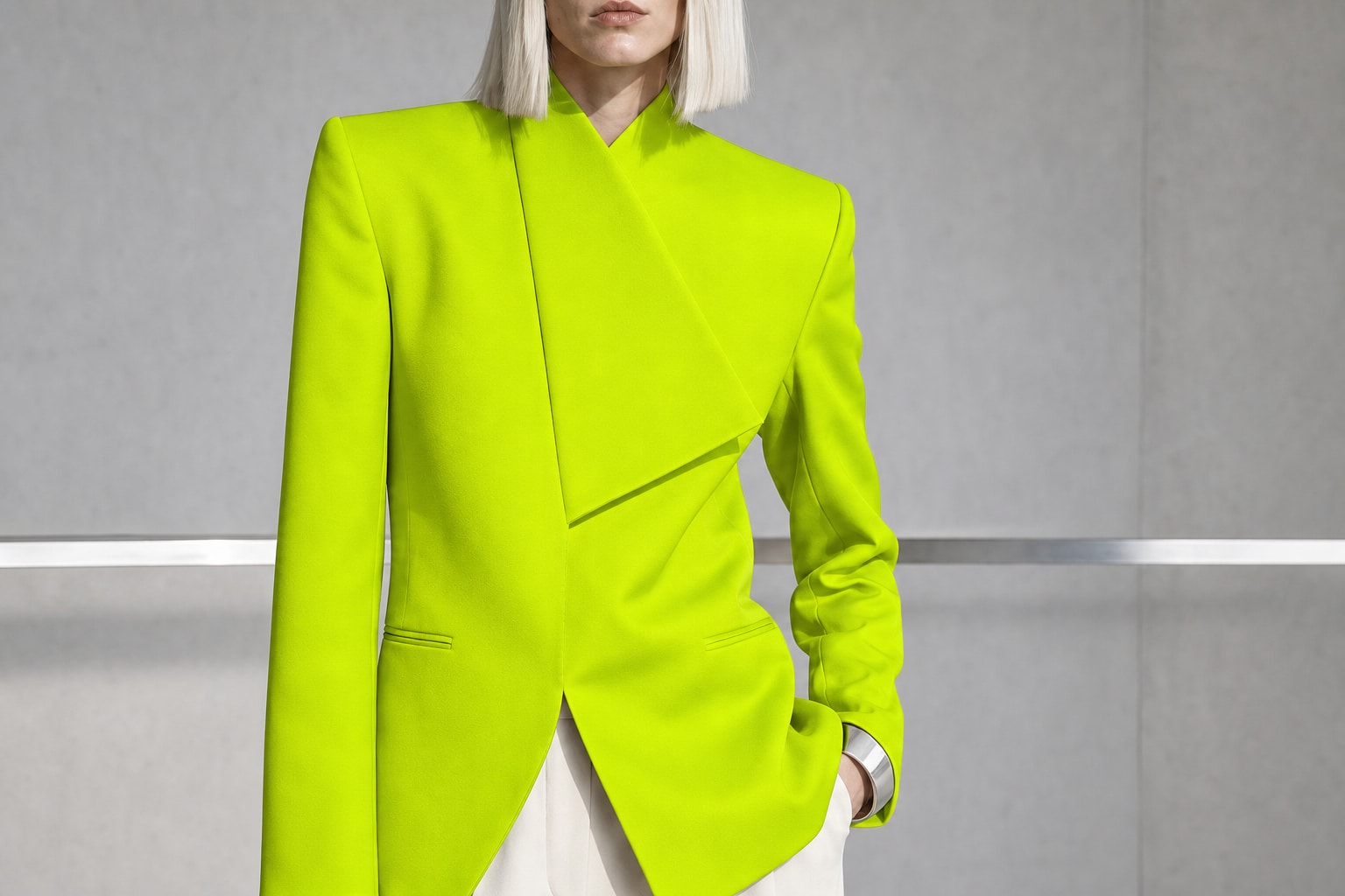 Fictional blonde fashion model in sculptural tailoring inside a concrete studio