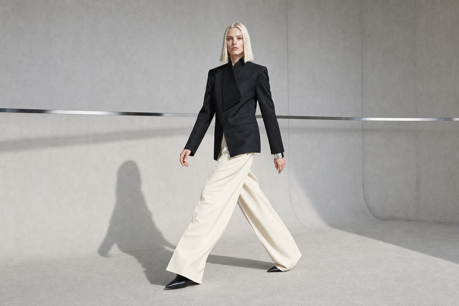 Fictional blonde fashion model in sculptural tailoring inside a concrete studio