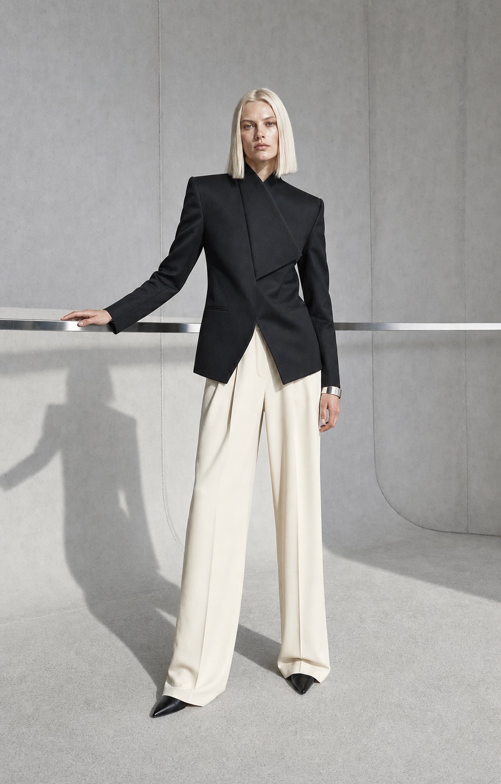 Fictional blonde fashion model in sculptural tailoring inside a concrete studio