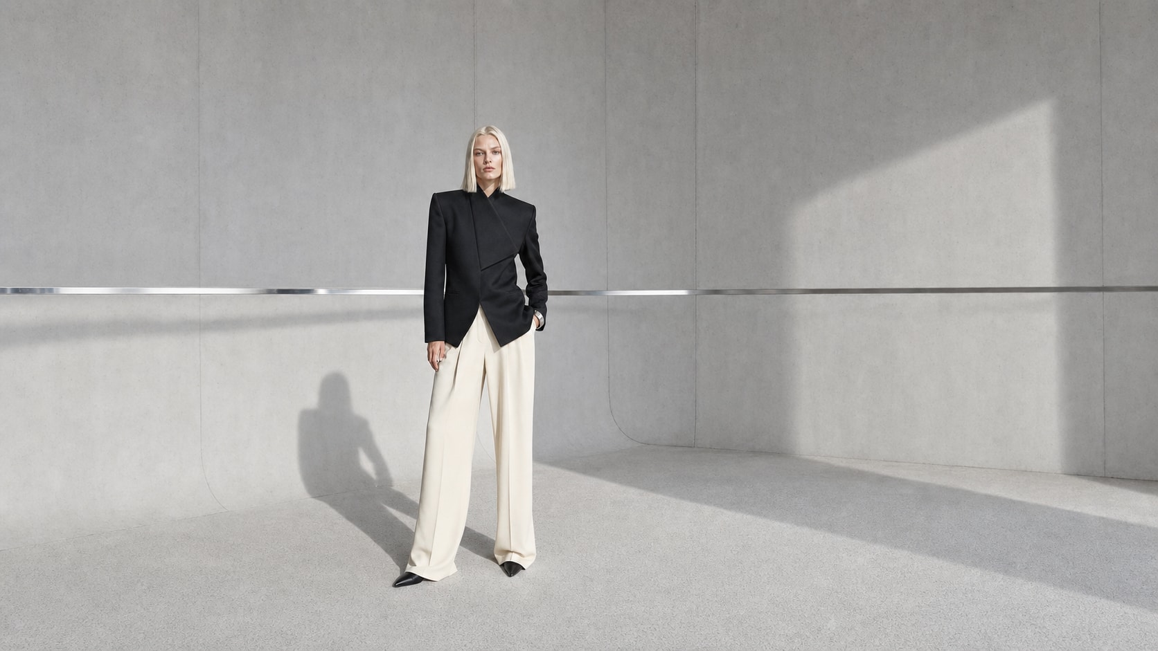Fictional blonde fashion model in sculptural tailoring inside a concrete studio
