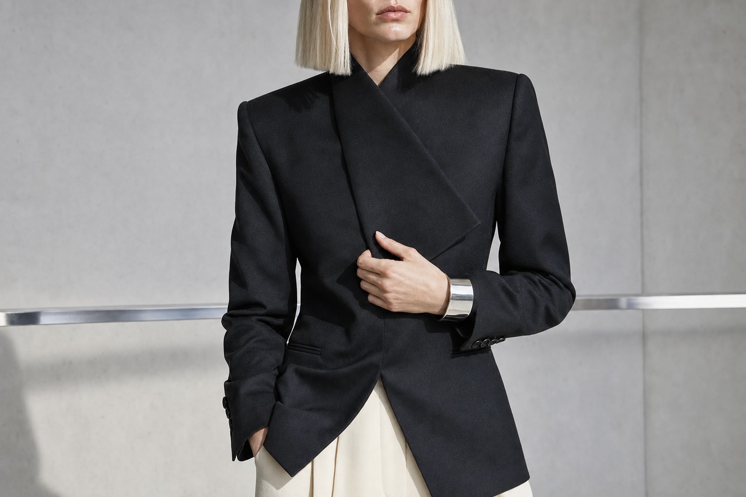 Fictional blonde fashion model in sculptural tailoring inside a concrete studio